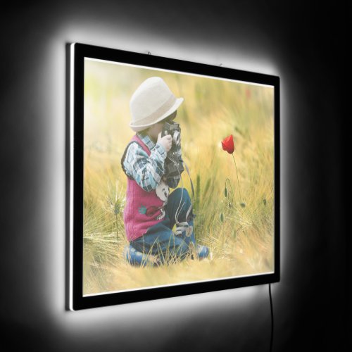 child kneeling in a field while holding a camera LED sign