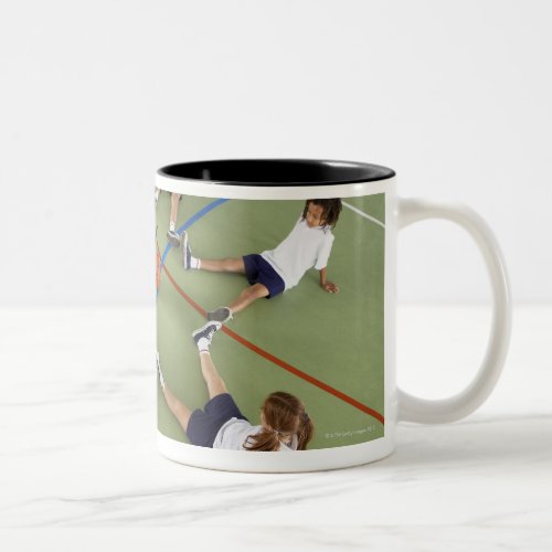 Children sitting on the floor of a sports hall Two_Tone coffee mug