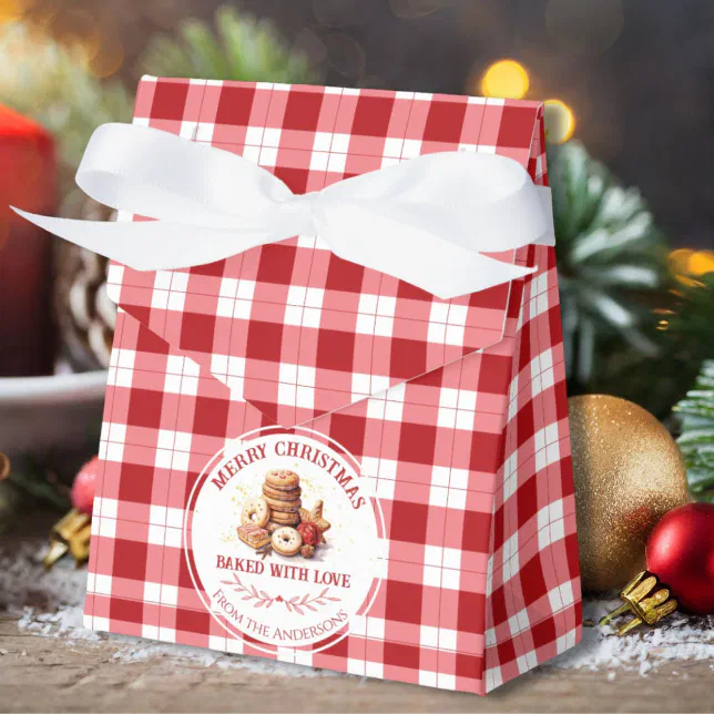A checkered Christmas favor box in red and white. Some Christmas decorations can be seen lying behind the favor box and there's a sticker with cookies displayed on the front of the box.