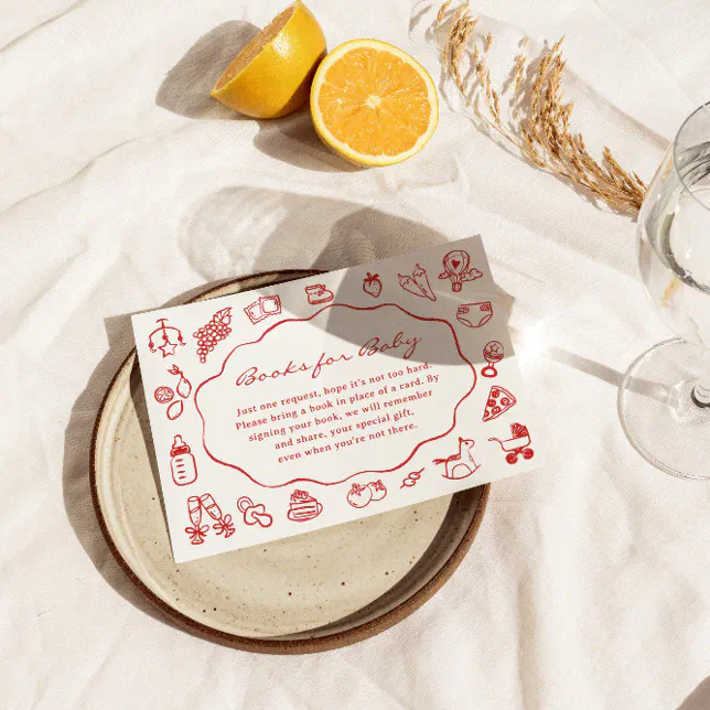 An enclosure card is placed on a ceramic plate, which is displayed on a linen tablecloth with a sprig of hay and a sliced orange displayed nearby.