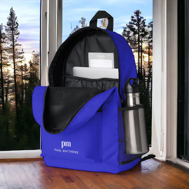 A blue backpack with a grey steel water bottle in the pocket sits next to a window with trees outside.
