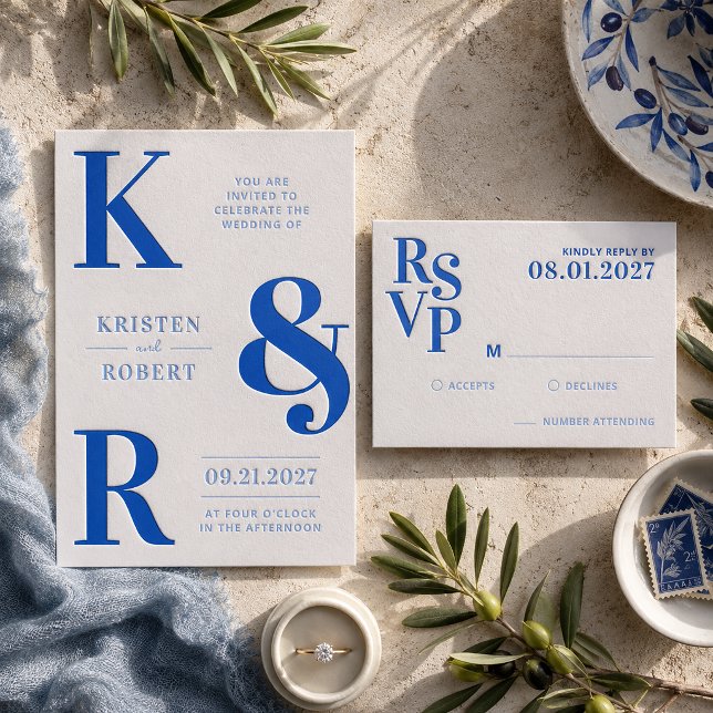 A collection of letterpressed wedding stationery with a bright blue color scheme. Leaves and plates are lying next to the RSVP and invite.