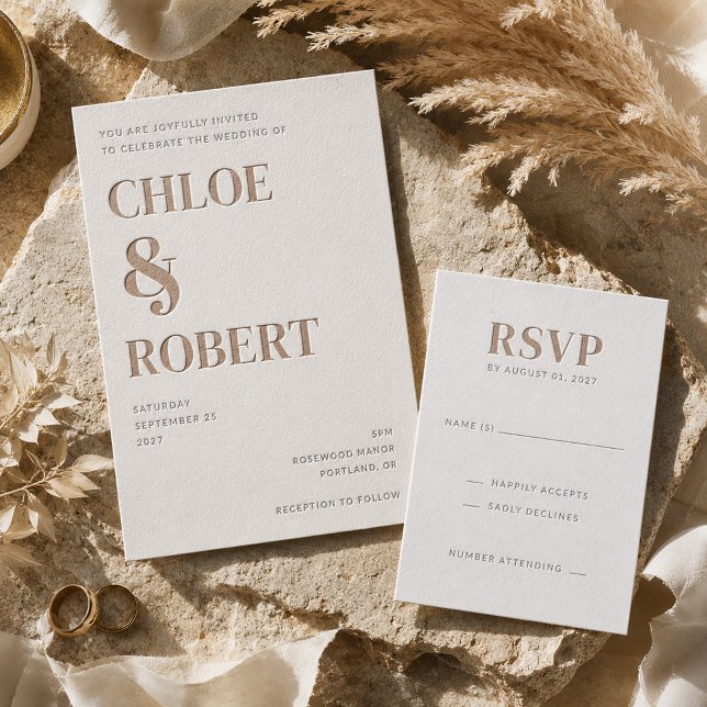 A collection of letterpressed wedding stationery with a gold blue color scheme. Wedding rings and foliage can be seen in the background. 