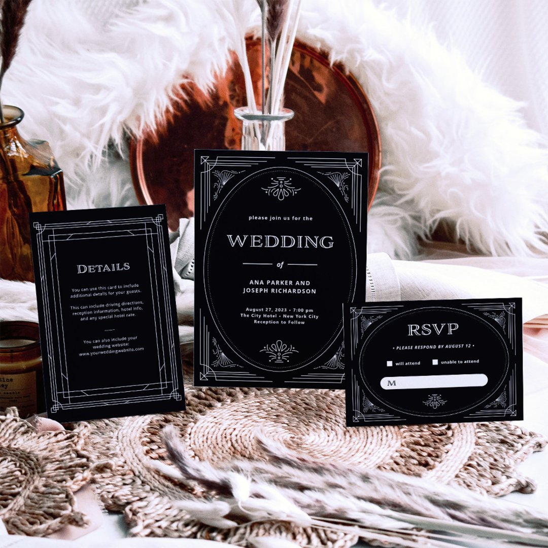 A black and white art deco wedding invitation suite with matching details and RSVP cards, styled on a woven placemat with a copper tray, amber glass bottles, and a fluffy white throw behind.