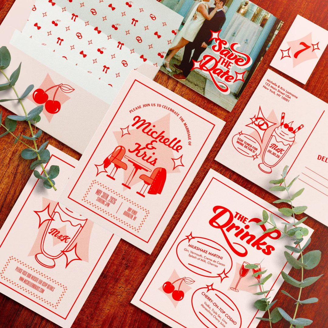 A red and white retro diner-themed wedding suite including an invitation, photo save the date, drinks menu, and table number, arranged on a wooden table with a cherry-print envelope liner and eucalyptus sprigs.