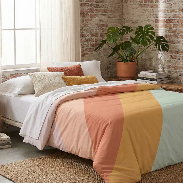 Colorful retro bedding is showing with a plant, some books, and a window in the background.