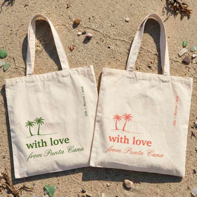 Two custom tote bags with palm tree motifs are shown laying on the sand on a beach.




