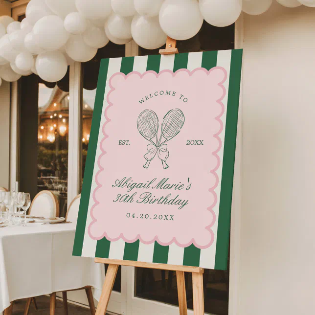 A tennis-themed sign with white balloons hanging above it. Table settings can be seen to the left. 