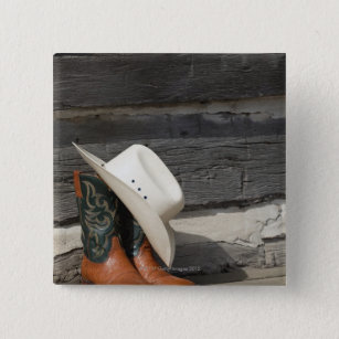 Cowboy hat on cowboy boots outside a log cabin pinback button