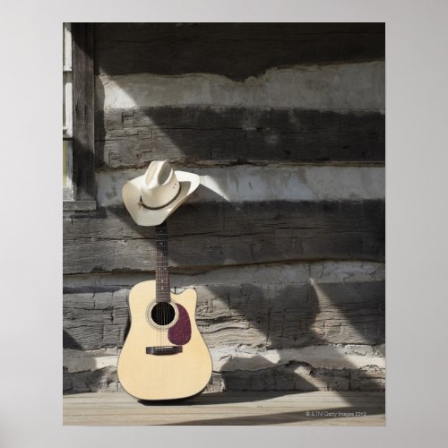Cowboy hat on guitar leaning on log cabin poster