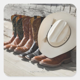 Cowboy hat on row of cowboy boots outside a log square sticker