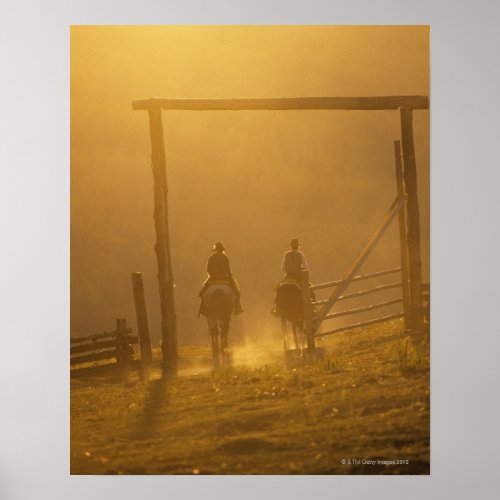 Cowboys riding through gate at dusk poster