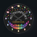 Crayons Stars Colorful Teacher's Name Classroom Round Clock<br><div class="desc">Kindergarten wall clock personalized with the teacher's name beneath colorful stars and above a row of crayons in a rainbow gradient with the numbers in bold white numbers outlined with the colors of the rainbow. Classroom wall clock with colorful crayons and stars against a black background. Teacher's wall clock personalized...</div>