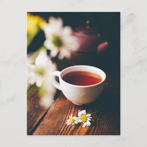 Cup of black tea and two chamomile flowers postcard
