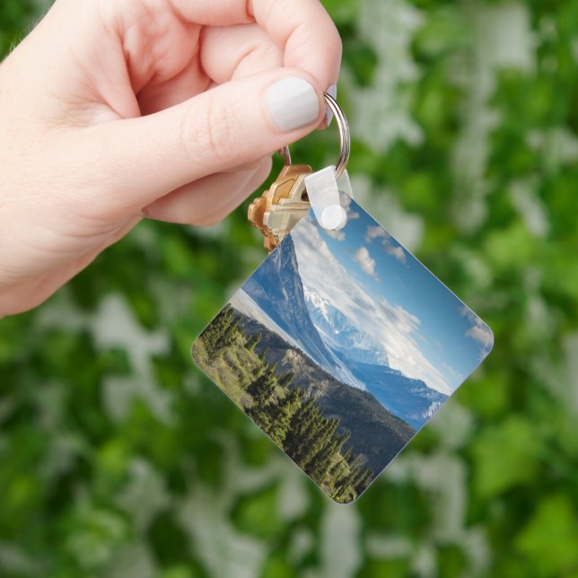 A hand is seen holding a keychain that contains a picture of a mountain range.