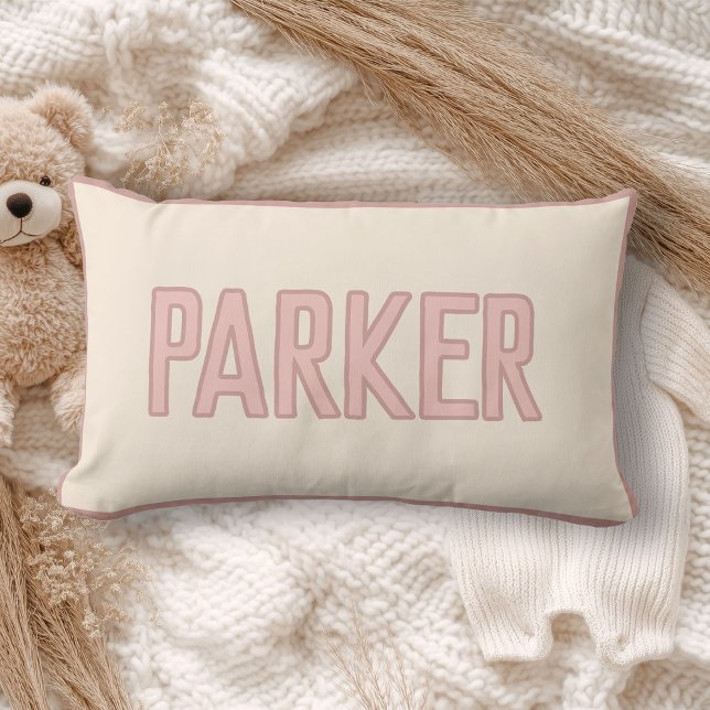 Cute Custom Kids Name with Faux Trim Pink Lumbar Pillow (A cream pillow with "WILDER" in light pink lettering lies on a cozy, soft-knit blanket)