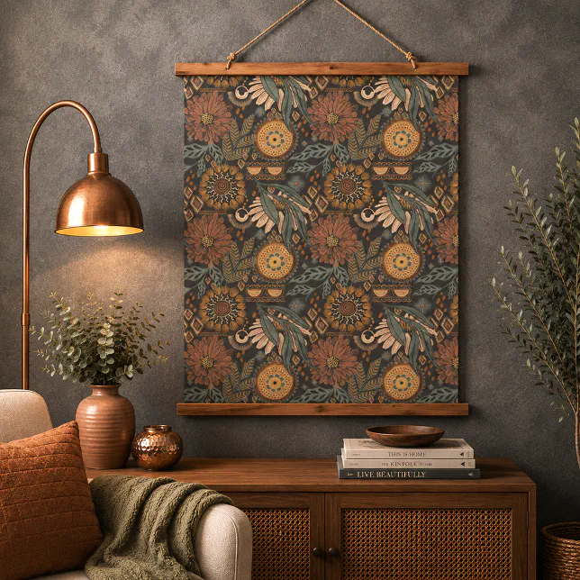 A dark boho tapestry above a small cupboard with a vase and some books placed on top. There is a sofa chair and a lamp to the left.