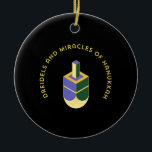 DREIDELS AND MIRACLES OF HANUKKAH CERAMIC ORNAMENT<br><div class="desc">This stylized illustration features a dreidel colored yellow, purple, and green against a stark black background. A curved gold text above it reads "DREIDELS AND MIRACLES OF HANUKKAH", highlighting the traditional toy and the spiritual celebration of the Jewish holiday. The design has a clean, geometric aesthetic with a touch of...</div>
