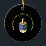DREIDELS AND MIRACLES OF HANUKKAH CERAMIC ORNAMENT<br><div class="desc">This stylized illustration features a dreidel colored yellow, purple, and green against a stark black background. A curved gold text above it reads "DREIDELS AND MIRACLES OF HANUKKAH", highlighting the traditional toy and the spiritual celebration of the Jewish holiday. The design has a clean, geometric aesthetic with a touch of...</div>