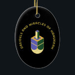 DREIDELS AND MIRACLES OF HANUKKAH CERAMIC ORNAMENT<br><div class="desc">This stylized illustration features a dreidel colored yellow, purple, and green against a stark black background. A curved gold text above it reads "DREIDELS AND MIRACLES OF HANUKKAH", highlighting the traditional toy and the spiritual celebration of the Jewish holiday. The design has a clean, geometric aesthetic with a touch of...</div>