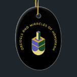 DREIDELS AND MIRACLES OF HANUKKAH CERAMIC ORNAMENT<br><div class="desc">This stylized illustration features a dreidel colored yellow, purple, and green against a stark black background. A curved gold text above it reads "DREIDELS AND MIRACLES OF HANUKKAH", highlighting the traditional toy and the spiritual celebration of the Jewish holiday. The design has a clean, geometric aesthetic with a touch of...</div>
