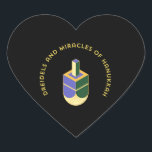 DREIDELS AND MIRACLES OF HANUKKAH HEART STICKER<br><div class="desc">This stylized illustration features a dreidel colored yellow, purple, and green against a stark black background. A curved gold text above it reads "DREIDELS AND MIRACLES OF HANUKKAH", highlighting the traditional toy and the spiritual celebration of the Jewish holiday. The design has a clean, geometric aesthetic with a touch of...</div>