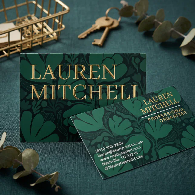 Deep green and navy blue organic botanical pattern business cards with large abstract leaves and prominent, metallic gold foil lettering. The card sits on a gold wire basket with a set of brass keys and a sprig of eucalyptus leaves surrounding it!