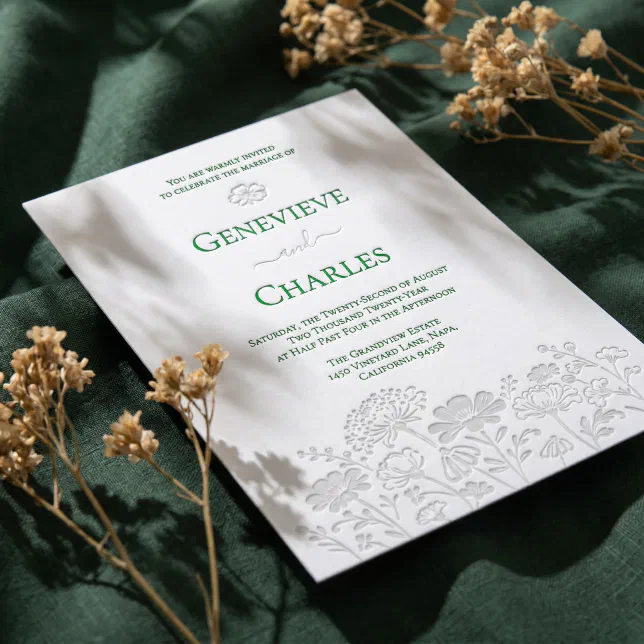 A beautiful letterpress wedding invitation sits on top of a green textured material. Yellow foliage can be seen in the background.