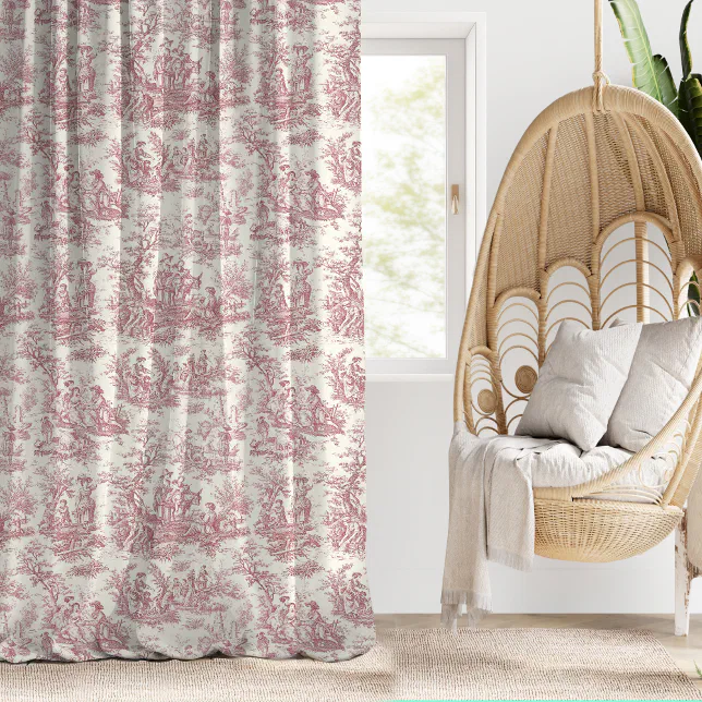 A red and white toile de joy printed curtain next to a wooden hanging chair with white cushions and a white blanket. 