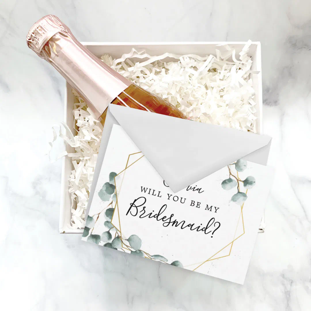 Eucalyptus greenery bridesmaid proposal card with botanical design sitting in a box with rose wine.