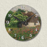 Farmhouse with Meadow Flowers  Round Clock<br><div class="desc">A charming countryside scene where a red-roofed farmhouse sits peacefully amid a sea of blooming meadow flowers. Hans Andersen Brendekilde captures the serene harmony between human dwelling and untamed nature. The field brims with vibrant red poppies, delicate white daisies, and soft grasses swaying in the summer breeze. His precise realism...</div>