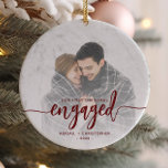 First Christmas Engaged Photo Red Script Ceramic Ornament<br><div class="desc">Commemorate your engagement with this beautiful modern keepsake ornament. The burgundy red text reads "Our first Christmas engaged, " with the word "engaged" in bold handwriting script with flourishes before and after. Replace the sample image with your favorite photo, and add your names and the year. A white gradient filter...</div>