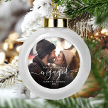 First Christmas Engaged Photo White Script Ceramic Ball Christmas Ornament<br><div class="desc">Commemorate your engagement with this beautiful modern keepsake ornament. The white text reads "Our first Christmas engaged, " with the word "engaged" in elegant handwriting script with flourishes before and after. Replace the sample image with your favorite photo, and add your names and the year. A dark gradient filter helps...</div>