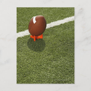 Football atop tee on football field, elevated postcard