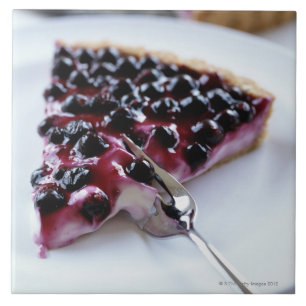 Fork slicing blueberry pie on plate tile
