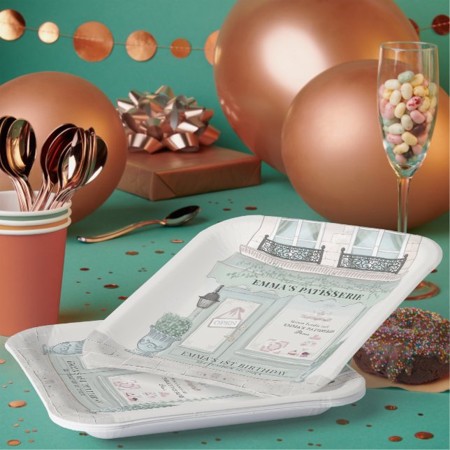 A French Patisserie shop front in a pale gree color with a wall lamp and outdoor plants. The background includes confetti, rose gold balloons, spoons and paper cups. There's a donut and champagne flute filled with colorful chocolate to the right.
