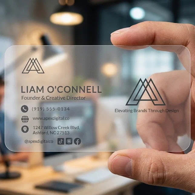 A frosted business card is held in a person's hand, with a desk partly visible behind it. 
