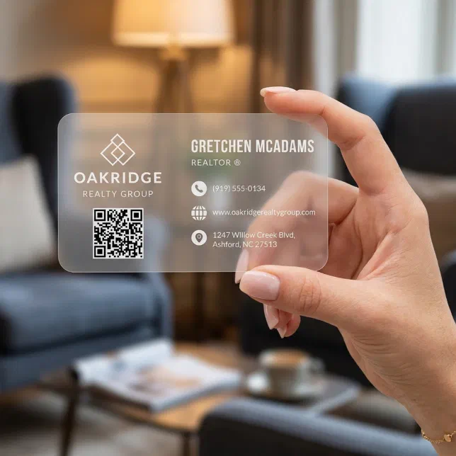 A person holds a frosted business card with a QR code. A couch and armchair can be seen in the background.