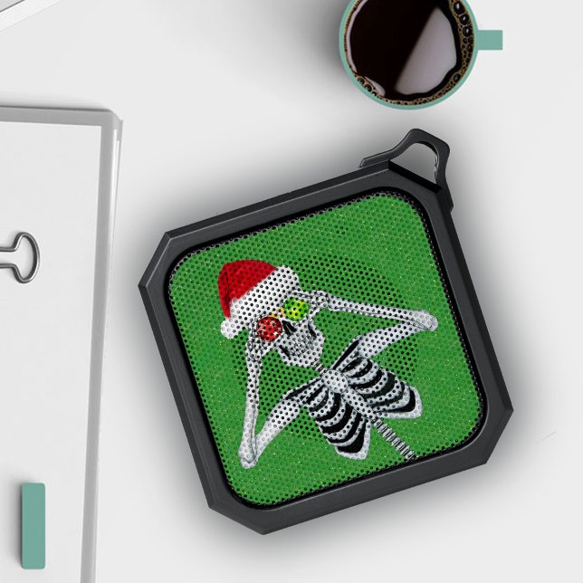 Funny Skeleton Holding Shiny Ornaments Santa Hat Bluetooth Speaker (Funny Christmas Skeleton Holding ornaments up to eyes Santa hat on green bluetooth speaker.)