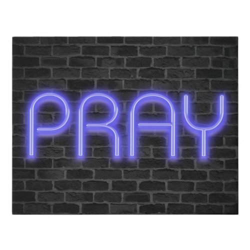 glowing neon PRAY sign on brick