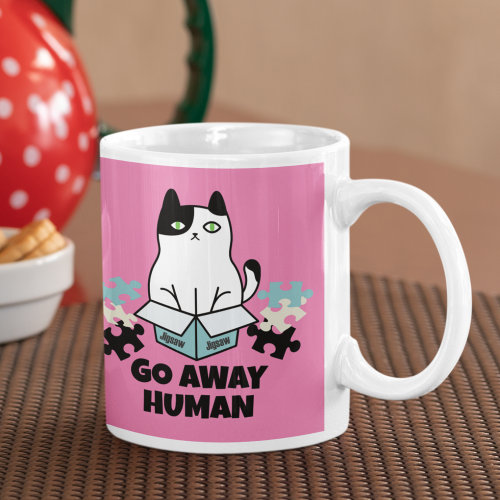A mug with a picture of a cat sat in a jigsaw puzzle box, the text says, go away human.