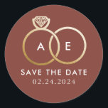 Golden Wedding Rings on Earthy Red Save the Date Classic Round Sticker<br><div class="desc">A modern monogram gets glam with intertwined golden wedding rings on a warm,  earthy red background and easy to personalize text for your initials,  wording and the wedding date to be saved.</div>