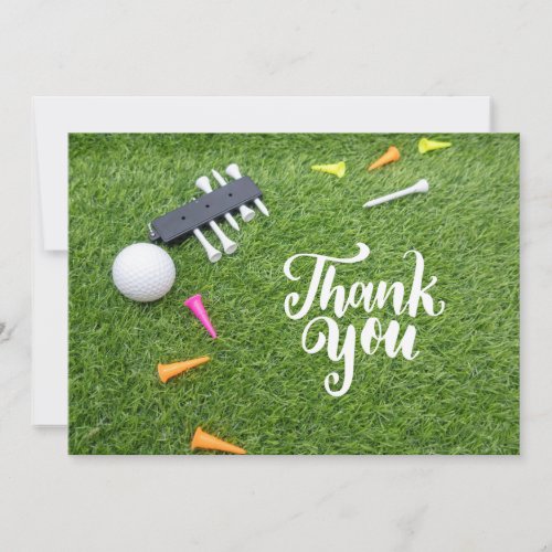 Golf ball and colorful tee on green grass thank you card