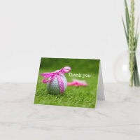 Golf ball with pink ribbon are on green grass thank you card