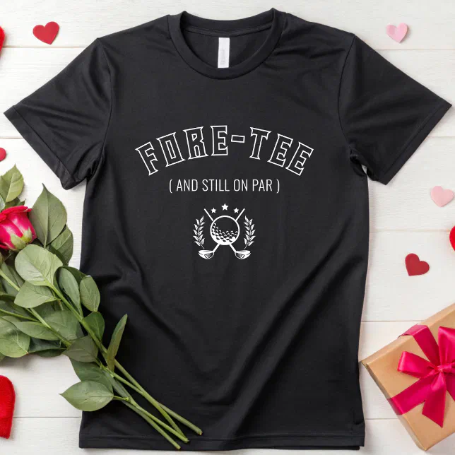 A golf-themed t-shirt with a pun is lying on a white surface. A red rose in on the left and a neatly packaged present is on the right. There are paper hearts strewn like confetti around the scene.