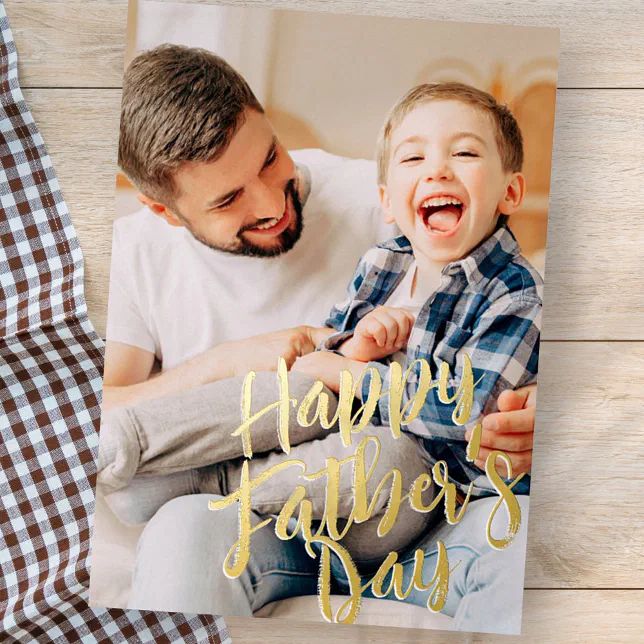 A Father's Day card with a father and son laughing and making faces. Fabric with a checkered pattern is lying underneath the card. 