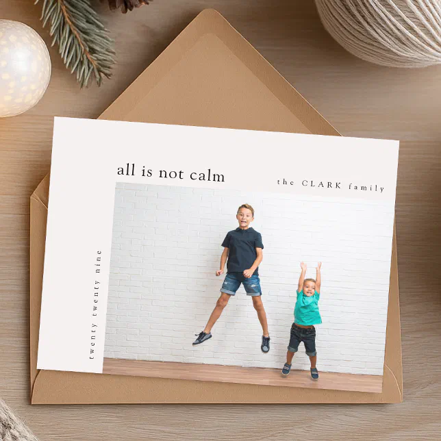 A photo holiday card resting on a brown envelope with a ball of yarn and some fir tree leaves in the background.