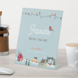 Holiday Town/Village Blue Baby Shower Favors Pedestal Sign<br><div class="desc">This cute "it takes a village/special delivery" Christmas holiday boy's baby shower favors pedestal sign features a light blue background with christmas lights and a holiday town/village. Personalize it for your needs. You can find matching products at my store.</div>