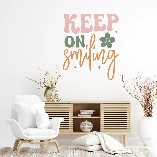 A peel-and-stick decal sticker on a wall, and pictured with it are a couple of plant vases, a white chair, a wooden shelving unit, and some white pillows and throws.