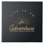 Life is an Adventure Explore Dream Discover Ceramic Tile<br><div class="desc">A ceramic tile with a gold colored illustration on a black-gray background. Designed with an illustration of a mountain with the suns rays shining outward from behind. Typography says: Life is an Adventure explore dream discover.</div>